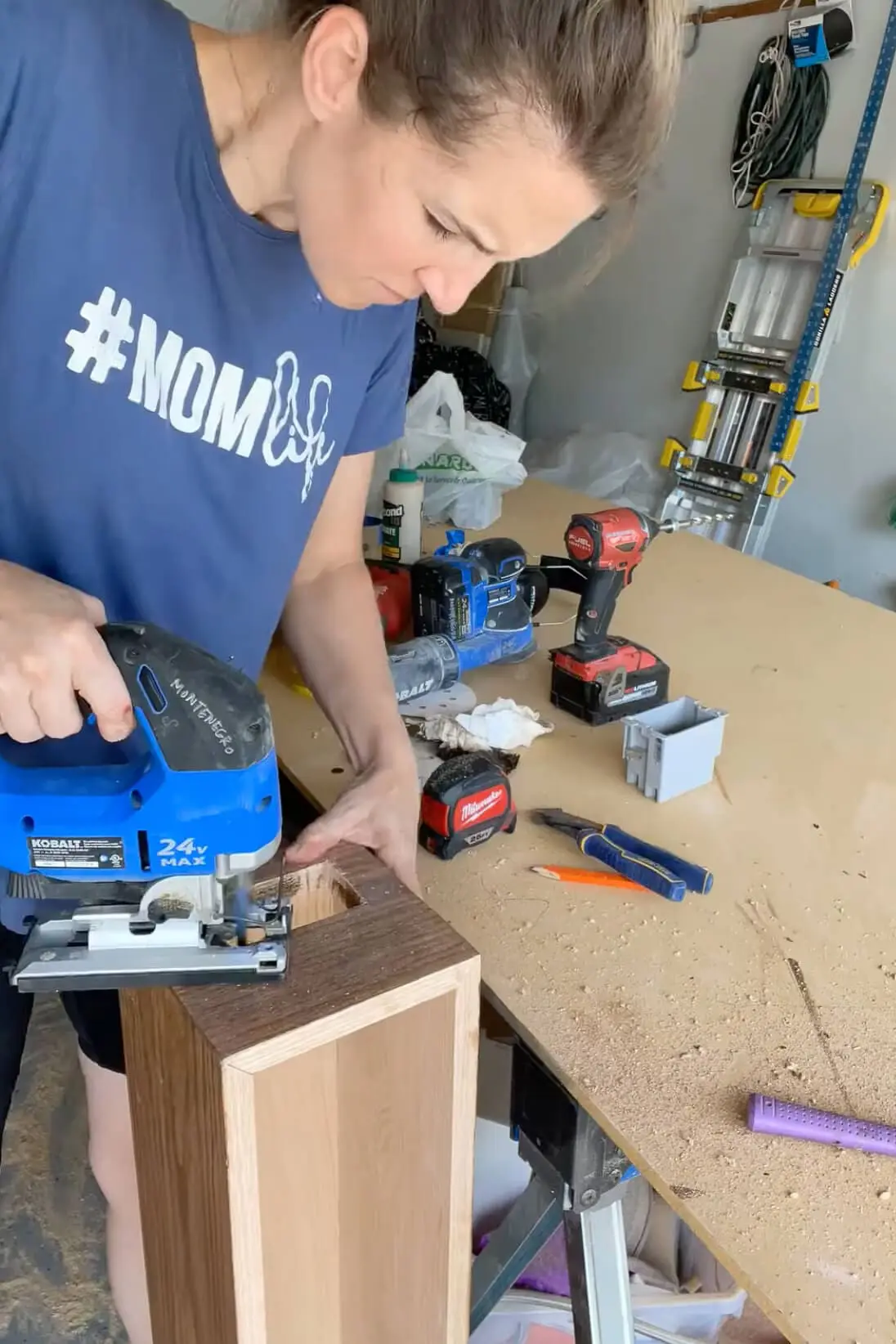 Cutting an opening in a DIY fireplace mantel for an electrical outlet using a jigsaw.
